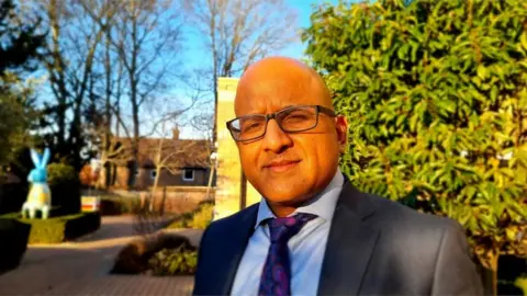 Paul Moseley/BBC Sanjay Kaushal dressed in a suit, wearing glasses, standing outside in daylight. He owns six care homes and is a director of the Norfolk Care Association