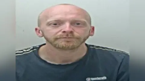Lancashire Constabulary Liam Slack is pictured in a police mugshot. He has a ginger beard and a bald head and is wearing a navy T-shirt with white stripes on the shoulders.