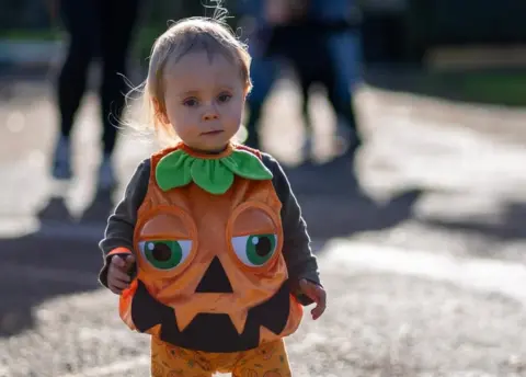 Peter Tranter Photography A toddler walking, wearing a pumpkin costume
