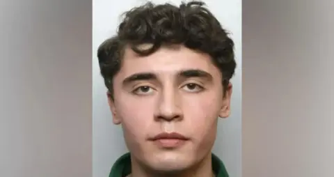 A mugshot of Daniel Khalife, who has short brown hair and thick eyebrows, wearing a green polo shirt 