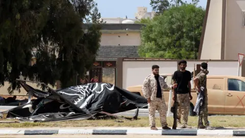 Getty Images Forces loyal to Libya's UN-backed unity government stand next to an Islamic State group flag in Sirte's centre in June 2016