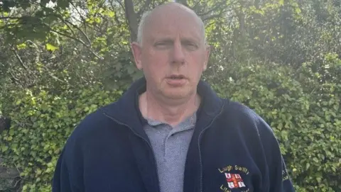 Joe Joyce, he has white hair and wearing a navy jacket that says Lough Swilly Lifeboat crew. He is wearing a grey polo shirt.