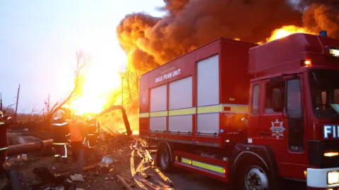 A fire engine and several firefighters at the scene of the Buncefield oil depot explosion in December 2005.