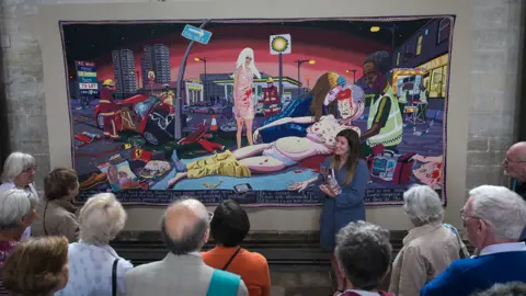 Finnbarr Webster A woman presenting a large tapestry to a group of cathedral visitors