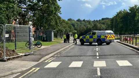 A police car and officers stood on a road and pavement at the university campus. 