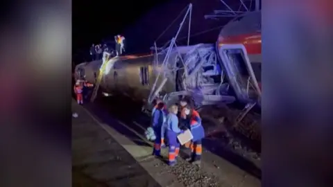 A still from video footage after a deadly train crash in Spain that shows emergency crews at the scene with authorities climbing onto the train