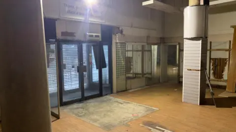 the ground floor of a vacant shop. the exit door is in the centre, with wooden floors and pillars close by