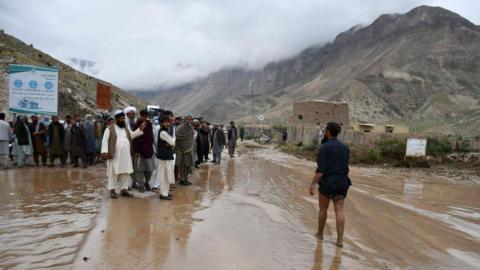 Afghans gather along a road between Samangan and Mazar-i-Sharif covered in mud following a flash flood after heavy rainfall
