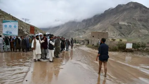 Getty Afghans gather along a road between Samangan and Mazar-i-Sharif covered in mud following a flash flood after heavy rainfall
