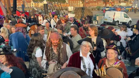 Auckland Shanty Singers A group of people dressed like pirates at a show presented by the Auckland Shanty Singers. The singers are mingling with the crowd.
