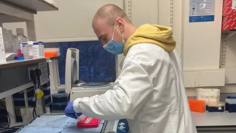 Rhys Brown Rhys at work in a lab coat and mask