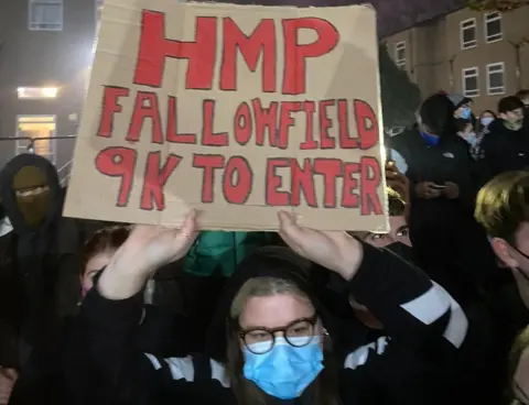 Ewan A student holds a sign reading "HMP Fallowfield, 9k to enter"