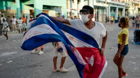 Getty Images A man waves a Cuban flag during a demonstration against the government of Cuban President Miguel Diaz-Canel in Havana