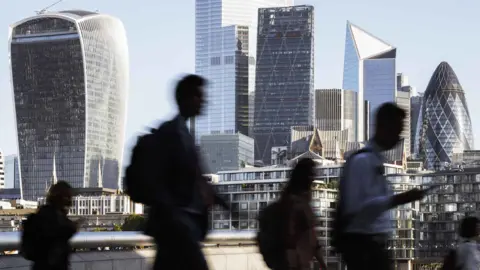 Getty Images People in silhouette walking by the bank of the Thames, with skyscrapers in the background