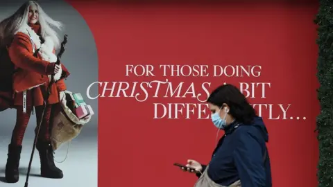 EPA Woman wearing mask walking past Christmas poster
