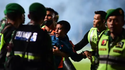 Getty Images - This picture taken on October 1, 2022 shows a boy (C) being carried as members of the Indonesian army secure the pitch after a football match between Arema FC and Persebaya Surabaya