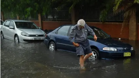 EPA A man wades through floodwater in Sydney, Australia