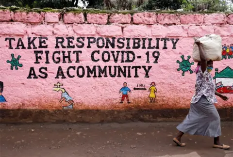 Reuters A woman walks past a mural whose slogan reads: "Take responsibility, fight against Covid-19 as a community."