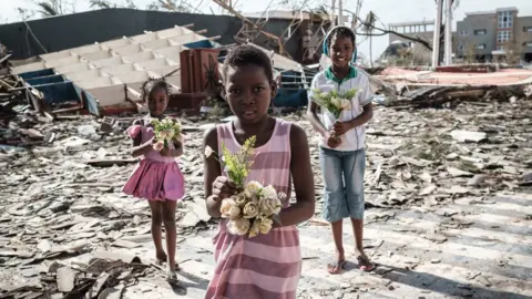Getty Images Girls collect artificial flowers from the rubble of a building destroyed by the cyclone Idai at Sacred Heart Catholic Church in Beira, Mozambique, on March 24, 2019.
