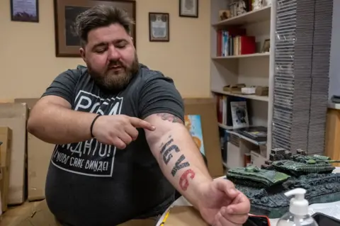 Andriy Kozinchuk, a military psychologist who serves at the front, points to a tattoo that means, 'I've got your back'