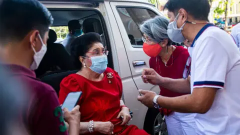 Getty Images Presidential Candidate Ferdinand "Bongbong" Marcos Jr. speaks to his mother, Imelda Romuandez Marcos, after casting his vote at the Mariano Marcos Memorial Elementary school which has been converted into a polling precinct on 9 May 2022 in Batac, Philippines