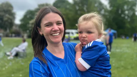 Alice Cunningham/BBC A woman in a blue Ipswich shirt holding her daughter, who is also in an Ipswich shirt.