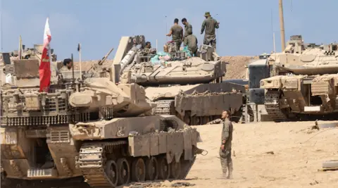 Amir Levy/Getty Images Israeli soldiers arrange equipment on several tanks in a very sandy environment.