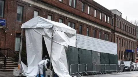 Getty Images A medical worker approaches a refrigerator truck being used as a morgue outside of Brooklyn Hospital Center amid the coronavirus pandemic on April 3, 2020 in New York City