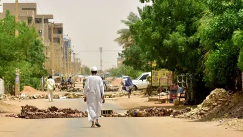 Getty Images Sudanese residents walk by barricades in Khartoum on June 9, 2019.