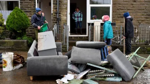 Getty Images Residents stand outside with ruined furniture in West Yorkshire