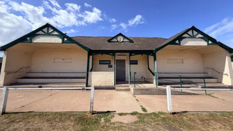 A view of the front of the pavilion. It has got white walls and green trimmings. 