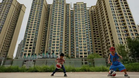 Getty Images Children play basketball in front of a housing complex by Chinese property developer Evergrande.