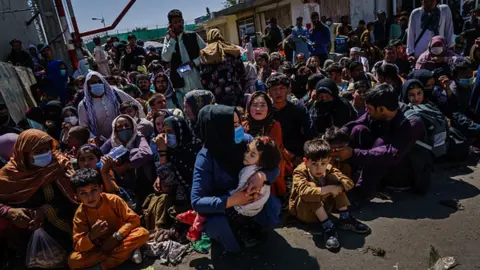 Getty Images Women and children wait outside the Taliban controlled check point near the entrance of the airport in Kabul, Afghanistan