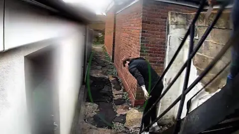 Hertfordshire Police A rear view of a man dressed in black making his way down a black stairway towards an alley