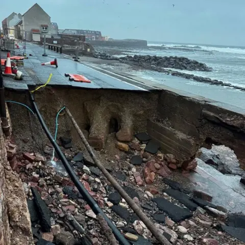 Laurence Gray A view of the sink hole in a road with exposed rock and cables.