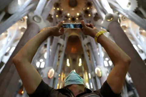 Reuters A man uses his phone as health workers, police officers and NGO staff members with their families visit the Sagrada Familia basilica as it reopens following the coronavirus disease (COVID-19) outbreak, in Barcelona, Spain, July 4, 2020