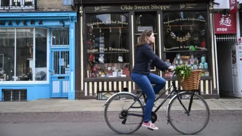 EPA Woman cycling past small shops in Cambridge