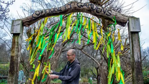 Ambitious PR A man tying yellow and green ribbons to an archway at Windmill Hill City Farm in Bristol