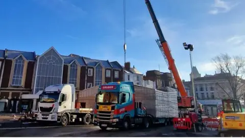 West Northamptonshire Council Stall on a lorry in the Market Square with a crane lowering its hook onto it