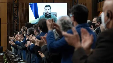 Getty Images TOPSHOT - Canadian Members of Parliament and invited guests applaud Ukrainian President Volodymyr Zelensky before virtually addressing the Canadian Parliament, March 15, 2022 in Ottawa