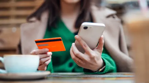 Getty Images Midsection of businesswoman making online payment with credit card and smartphone at side walk cafe