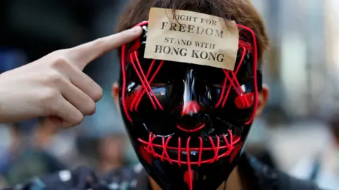 Reuters A masked anti-government protester points to a sign on his forehead which says "stand with freedom, stand with Hong Kong"