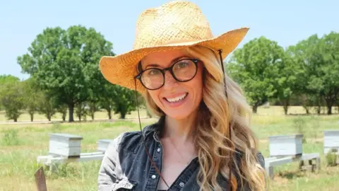 Erika Thompson, wearing a straw hat, poses in a field