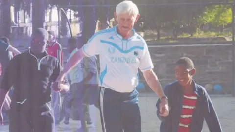 Judith Gates Bill Gates as an old man plays football with African children