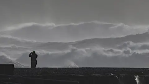 PA Media A person photographs high waves in Doolin in County Clare on the west coast of Ireland.