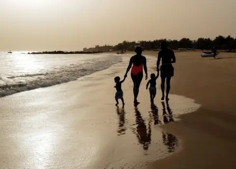 Reuters A man, woman and twin boys dressed in bathing suits walk along a beach.