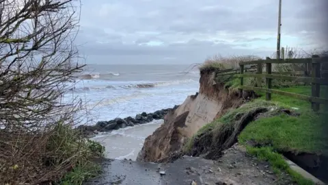 ANDREW TURNER/BBC A fence hangs in mid-air after erosion caused the cliff to collapse.