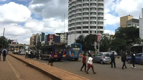 Pedestrians cross the six lane University Way in Nairobi, disregarding the footbridge (in the background)