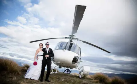 Alpine Images Kristy and Corey in the wedding outfits pose in front of a white helicopter