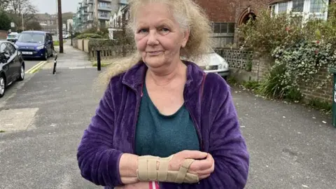 Christina Marchand standing where she was hit in Whitehawk by an e-bike. She is wearing a wrist support 